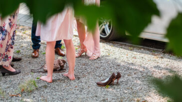 Photograph showcasing a social gathering outdoors. Focus on the lower body of people wearing formal attire with some barefoot, set amidst a natural and casual environment.