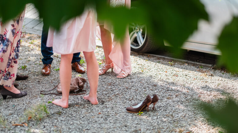 Photograph showcasing a social gathering outdoors. Focus on the lower body of people wearing formal attire with some barefoot, set amidst a natural and casual environment.