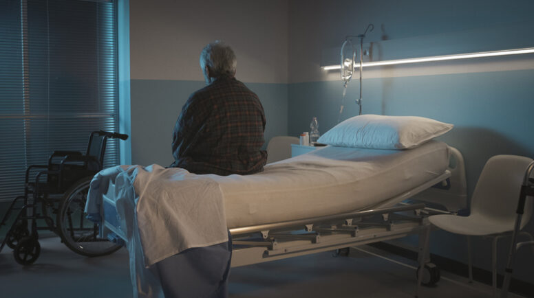 Depressed senior man sitting on the hospital bed alone at night, he feels lonely and abandoned