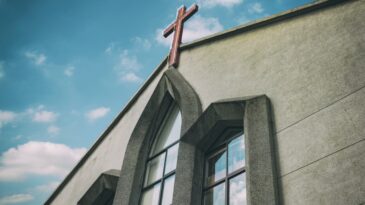 Gray church building with a cross outlined by blue sky