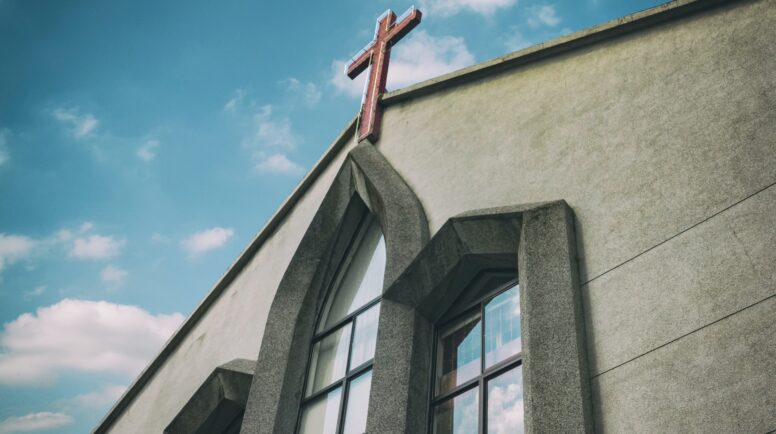 Gray church building with a cross outlined by blue sky