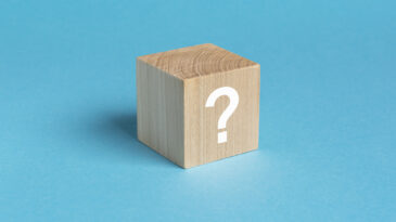 wooden toy cube with a question mark viewed high angle on a blue background with copy space in a conceptual image