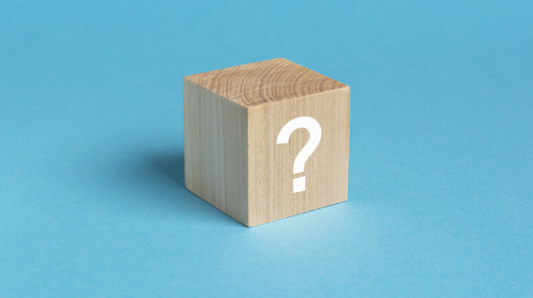 wooden toy cube with a question mark viewed high angle on a blue background with copy space in a conceptual image