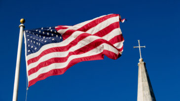 American flag and church steeple against very clear blue sky
