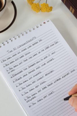 Ten commandments, a handwriting on notebook with a closed Holy Bible Book, and a cup of coffee on white background. Vertical shot, a close-up. Christian Law, obedience, and faith in God Jesus Christ. 