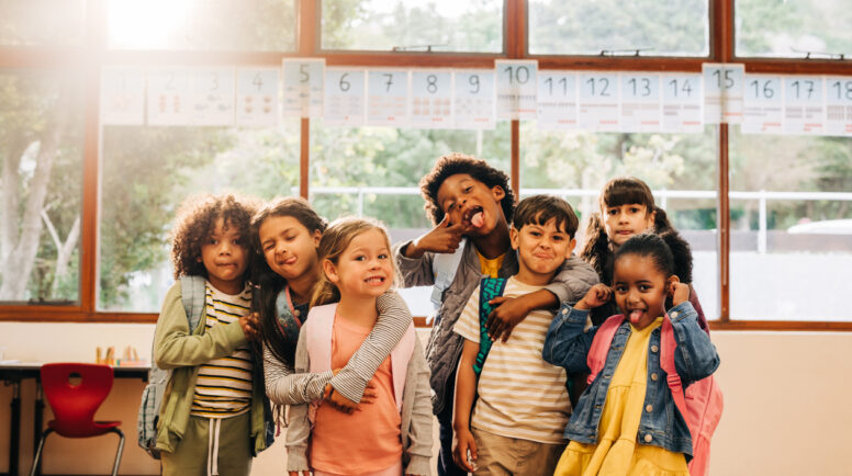 Young students stand together in a classroom, looking at the camera with funny faces. Kids excited to be back in school for a new year of childhood education. Children schooling in a diverse school.