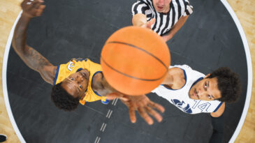 Basketball Tournament Final: Diverse Yellow and White Teams Compete at Center Court for Jump Ball that Starts the Game. Athletic Sportsmen Reach for the Ball. Top Down Cinematic Shot.