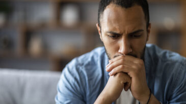 Closeup Portrait Of Thoughtful Black Young Man Sitting On Couch At Home, Pensive Worried African American Male Resting Chin On Hands And Looking Away, Depressed Guy Thinking About Life Problems