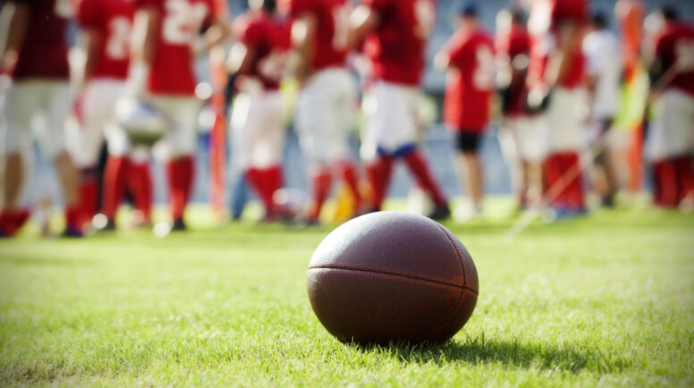 Close up of an american football on the field, players in the background
