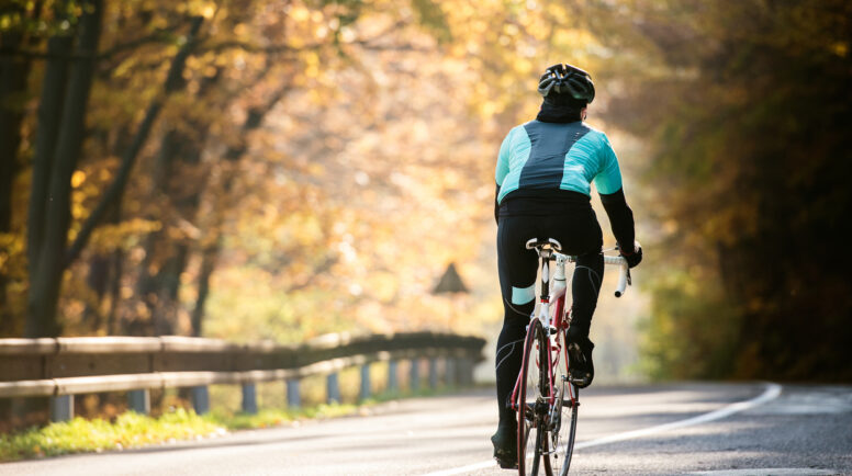 Young sportsman riding his bicycle outside in sunny autumn nature, rear view