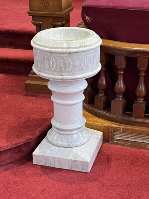 A white marble baptismal font in a sanctuary.