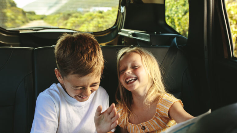 Small boy and girl sitting on backseat of car looking at map and smiling. Kids traveling in a car on roadtrip playing with a map.