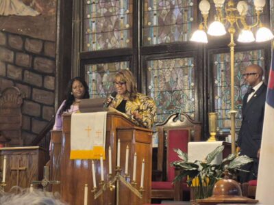 Three women stand behind a pulpit.