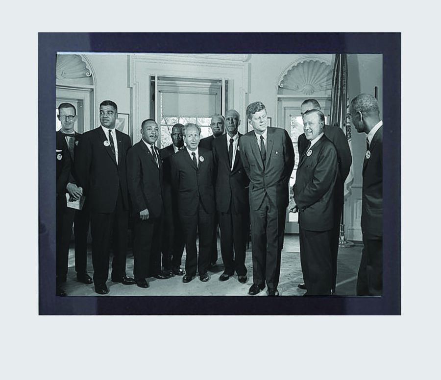 A black and white photo taken in the Oval Office during the Kennedy administration. Those featured in the picture include Martin Luther King Jr., John Lewis, President John F. Kennedy and Vice President Lyndon B. Johnson among others.