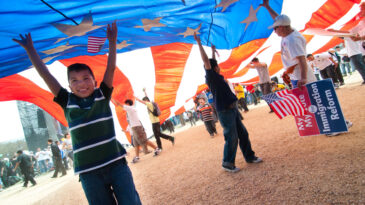 "Washington, DC, USA - March 21, 2010: Children play under a giant American flag as some 200,000 immigrants' rights activists flood the National Mall to demand comprehensive immigration reform."