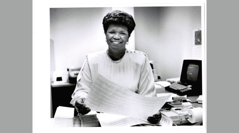A black and white photo of a woman smiling while working at a desk.