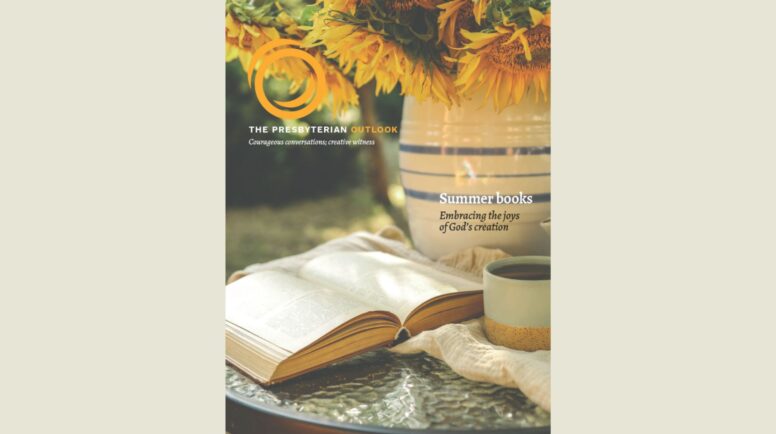 An open book, a vase of sunflowers and a mug on a table.