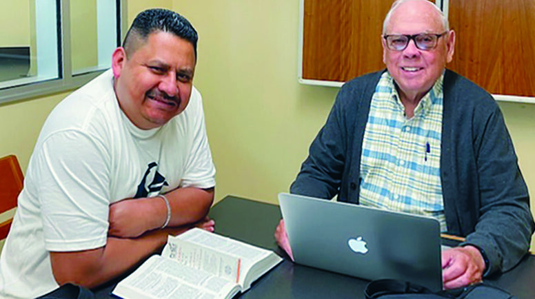 Jose and Don sat at a table with a laptop and book, meeting for their weekly conversation.