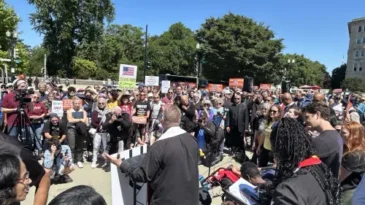 The Rev. Tony Larson opens Moral Monday event with a prayer. Pastor prays in front of a crowd.