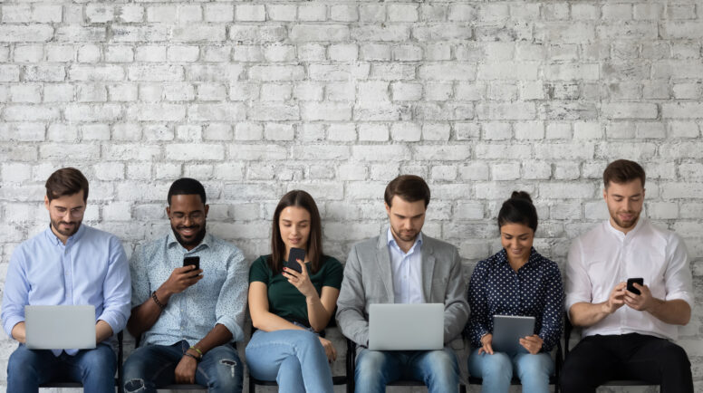 Multicultural team of gadget users sitting in line, using laptops, tablets, mobile phones, working, reading messages, chatting online on social media, watching content on internet.