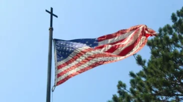 American flag on a flagpole that has a cross at the top