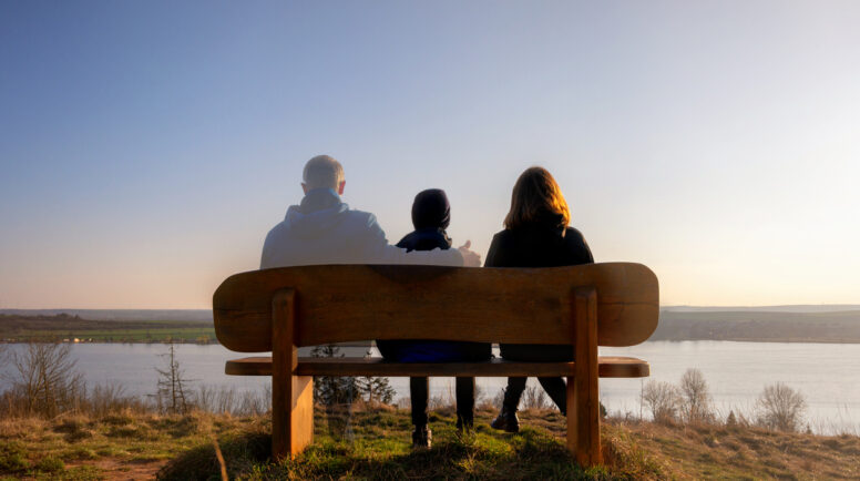symbolic image of death where three people are sitting on a bench but one is transparent