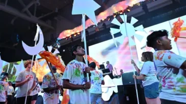 A group of youth walk around in a large convention center room holding celestial props.