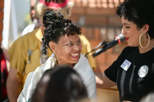 Two women stand on a podium. One woman is wrapped in a blanket and smiling, looking at the other woman.