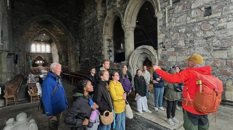 A group of Presbyterian College students stands in a old, stone church listening to a tour guide.