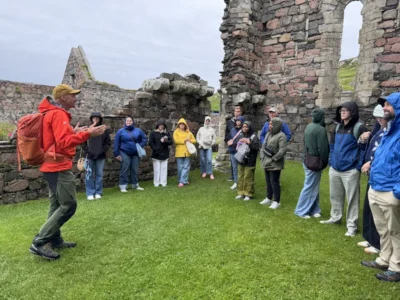 A group of college students stand outside with church ruins in the background.