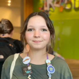 A young woman in a green shirt with a lanyard with many buttons