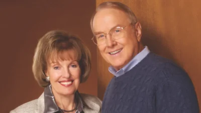 A white man with gray hair and glasses stands next to a woman with short brown hair. Both are smiling.