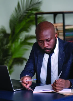 Young African executive reading documents and working on a laptop while sitting at his desk in an office