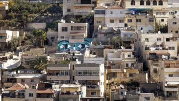 On a hillside with houses, a mural of two large eyes stands out.