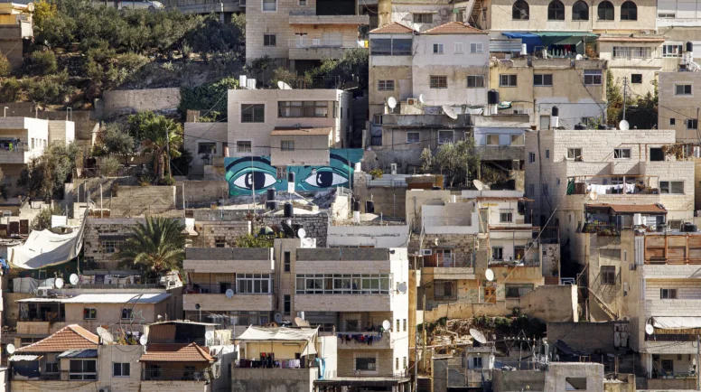 On a hillside with houses, a mural of two large eyes stands out.