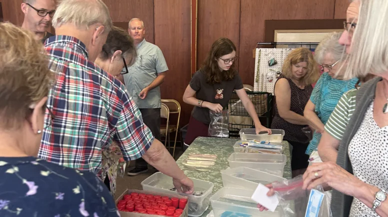 Church members gather around a table stacked with goods to make toiletry bags.