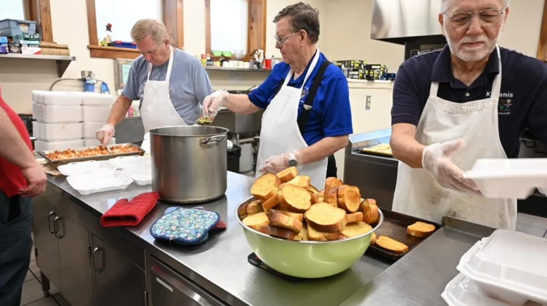 A group of men serve food in an industrial church kitchen.