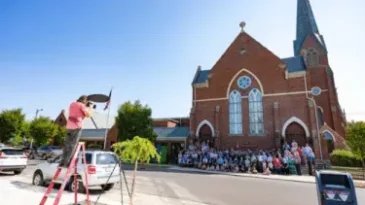 A photographer takes a picture of First Presbyterian Church of Columbus, Indiana with the congregation standing in front of the building.