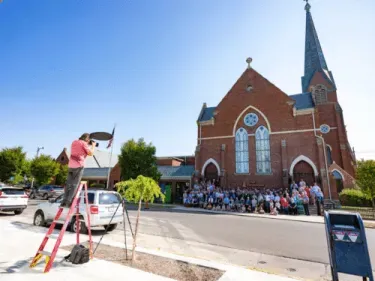 A photographer takes a picture of First Presbyterian Church of Columbus, Indiana with the congregation standing in front of the building.