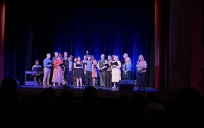 A group of people gathered on stage, holding sheet music and singing.