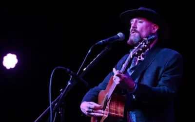 A man sings on stage with a guitar. 