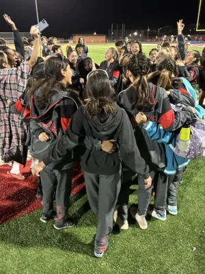 A group of students huddles on a football field, embracing.
