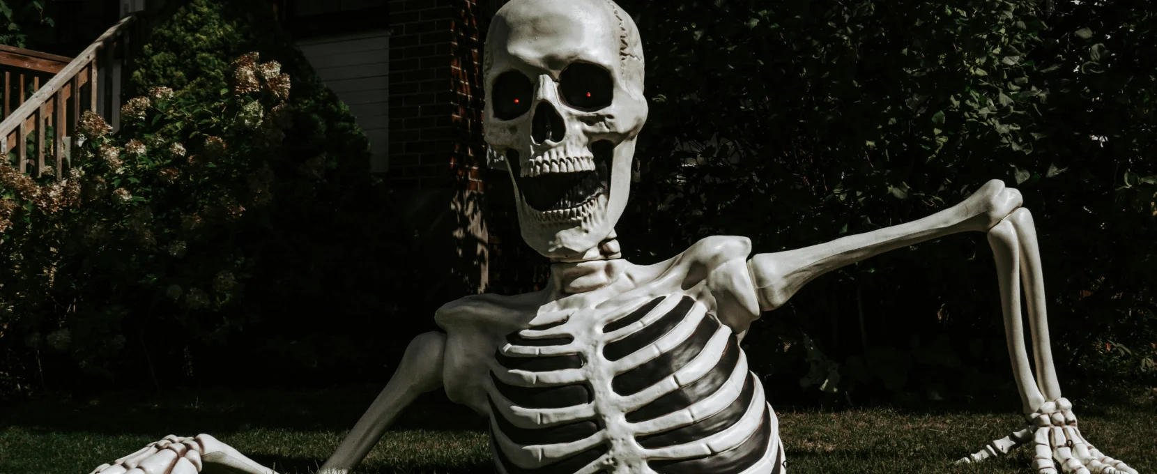 A large skeleton looks like it is climbing out of the ground in front of a house