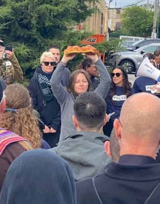 A pastor in a crowd raises a loaf of bread above her head.