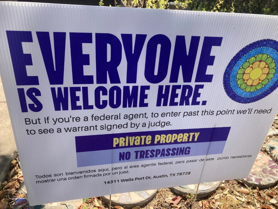 “Everyone is welcome here” in large letters. Underneath, in smaller type, the sign says: “But if you’re a federal agent, to enter past this point we’ll need to see a warrant signed by a judge.” 