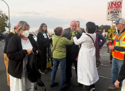 The Rev. Jorge Bautista, center, is helped after being hit with a pepper round during a protest on Oct. 23, 2025, in Oakland, Calif. (Photo courtesy of Leah Martens)