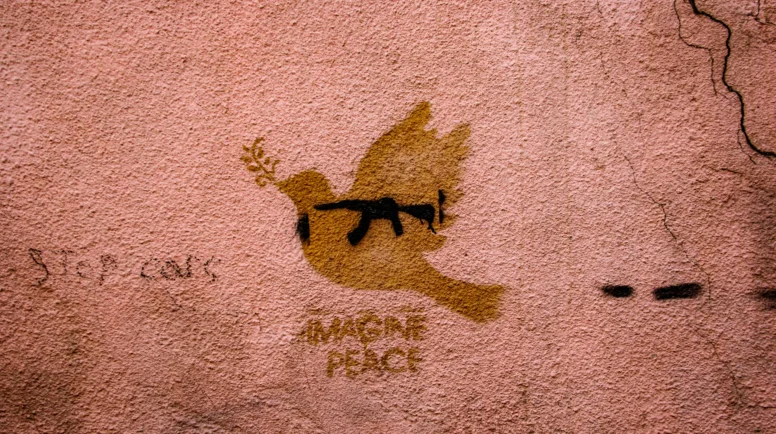 a spray paint dove on a wall on top of a gun. "imagine peace" is written underneath.