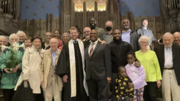A diverse group of people stand at the front of a sanctuary around pastor David Black.