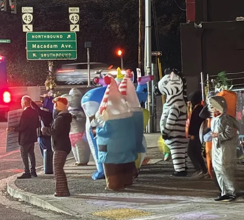 A group of protesters stand on a corner, some in inflatable animal costumes