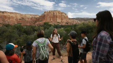 A Ghost Ranch staff person gives a tour to a group of children and parents. A mountain stands in the background.